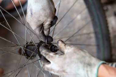 Bisiklet tekerleğinin aksı, koruyucu eldiven giyen yetenekli bir pratisyen tarafından deliniyor. Yağ lekeleri tekerlek rulmanlarına ekleniyor. Taylandlı tamirci