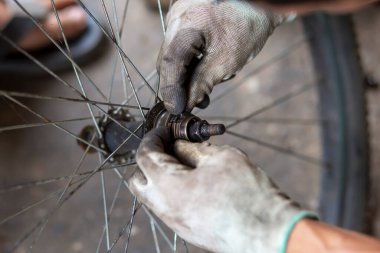 Bisiklet tekerleğinin aksı, koruyucu eldiven giyen yetenekli bir pratisyen tarafından deliniyor. Yağ lekeleri tekerlek rulmanlarına ekleniyor. Taylandlı tamirci