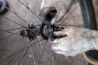Bisiklet tekerleğinin aksı, koruyucu eldiven giyen yetenekli bir pratisyen tarafından deliniyor. Yağ lekeleri tekerlek rulmanlarına ekleniyor. Taylandlı tamirci