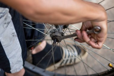 Bisiklet tekerleğinin aksı, koruyucu eldiven giyen yetenekli bir pratisyen tarafından deliniyor. Yağ lekeleri tekerlek rulmanlarına ekleniyor. Taylandlı tamirci