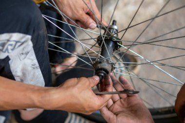 Bisiklet tekerleğinin aksı, koruyucu eldiven giyen yetenekli bir pratisyen tarafından deliniyor. Yağ lekeleri tekerlek rulmanlarına ekleniyor. Taylandlı tamirci
