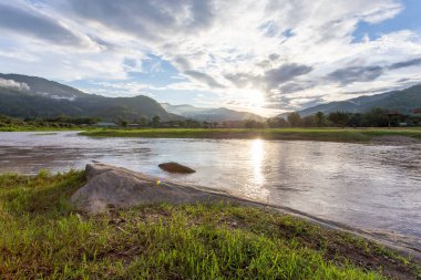 Dağ manzarası, gün batımı, sis, dağdaki yağmurdan sonraki bulutlar, berrak gökyüzü, nehir, açık yeşil çimenler, arka planda serin ve ferahlatıcı bir his verir.
