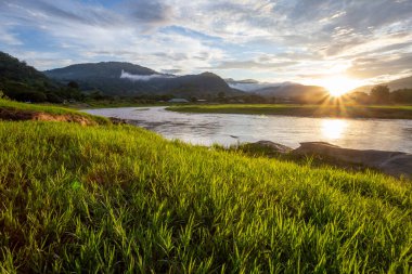 seçici odak noktası açık yeşil çimenler nehir dağı manzarası günbatımı sis bulutları dağ yağmurları açık gökyüzü açık nehir açık yeşil çimenler serin, ferahlatıcı bir duygu verir arka planda