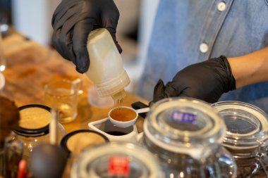 Seçici odaklanma, Honey beyaz bir ölçü kabına dökülüyor. İçkileri karıştırmak için dükkandaki personelin elinden tatlı, güzel kokulu, taze, sağlığa iyi gelen içkiler ekleyin..