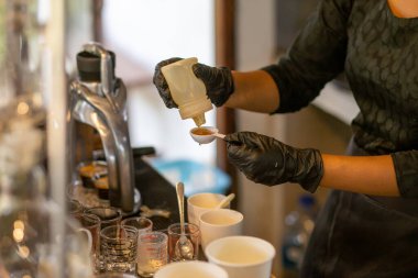 Seçici odaklanma, Honey beyaz bir ölçü kabına dökülüyor. İçkileri karıştırmak için dükkandaki personelin elinden tatlı, güzel kokulu, taze, sağlığa iyi gelen içkiler ekleyin..