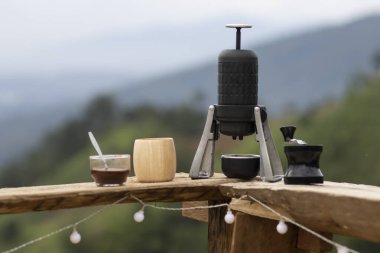 Seçici odaklı siyah manuel kahve makinesi, kahve ekipmanlarını ahşap balkon arka planına seriyor.