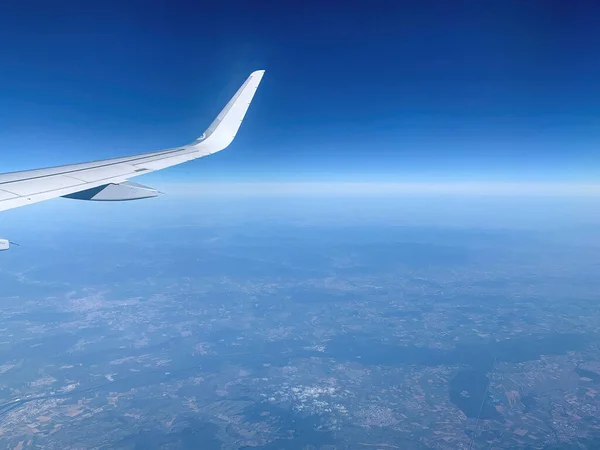 Airplane Window view on white wing and Earth and infinite horizon by clear sunny weather from high altitude