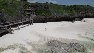 drone footage of a woman walking on the sandy beach, next to the green island