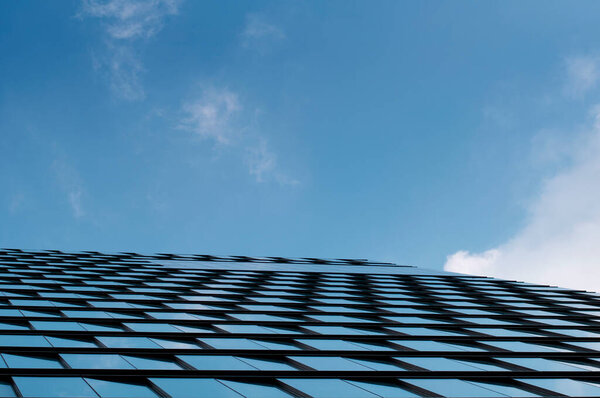 An abstract image of a modern skyscraper's windows against a blue sky with white clouds. the blue sky is reflecting off of the windows.
