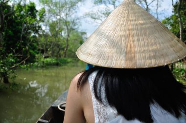 Geleneksel Vietnam hasır şapkası (Non la) takan Çinli bir kadın Mekong Nehri deltasındaki bir mangrov ormanında yüzüyor..