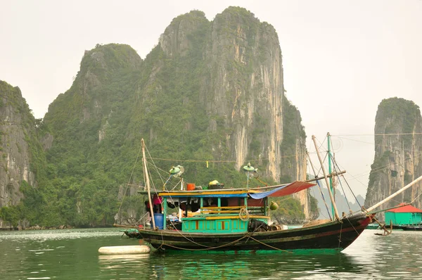 在阴天 一艘木船停泊在越南哈龙湾水域内独特的岩层和岛屿附近 — 图库照片
