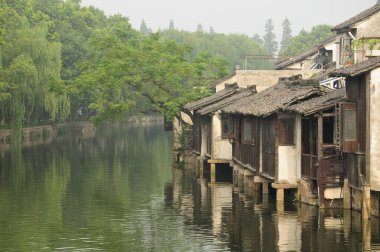Tahta, yıpranmış binalar sabahın erken saatlerinde Çin 'in Zhejiang eyaletinin doğu manzaralı tongxiang wuzhen kasabasındaki su kanallarını kaplıyor..   