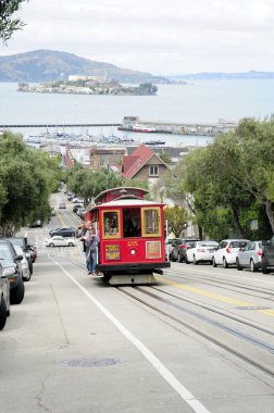 22 Mayıs 2016. San Francisco, Kaliforniya. Arka planda Alcatraz adası olan dik bir caddede yürüyen ünlü Hyde Tramvayı 'na binen turistler.  