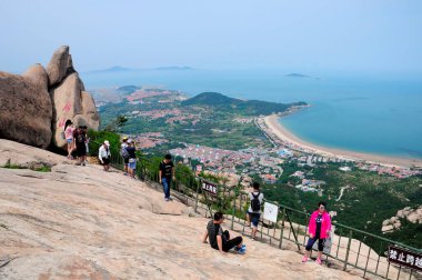 26 Haziran 2016. Qingdao, Çin. Çinli turistler Çin 'in Shandong eyaletindeki Qingdao şehrinde Laoshan (Lao Dağı) zirvesinde, doğu denizi ve kıyı kenti ise arka planda yer alıyor..   