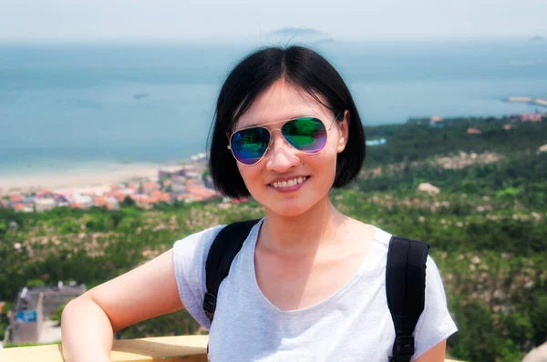 中国青岛市 一位笑容满面 戴着太阳镜的中国妇女 背靠东海 站在老山的一个旅游区 — 图库照片