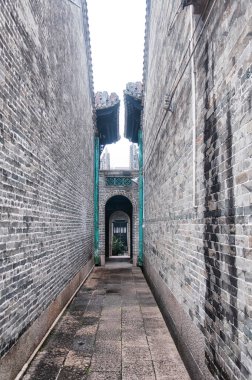 A narrow alleyway leading to an arch and doorway in the huangpu village scenic area of Guangzhou China on an overcast day. 