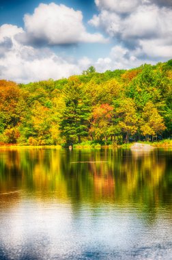 Fall foliage in autumn reflecting against the waters of Burr Pond State Park in Torrington Connecticut on a sunny blue sky day.  