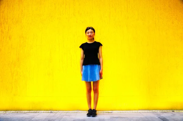 一名中国妇女穿着斜纹棉布短裙和黑色衬衫 站在一面黄色的墙壁前 — 图库照片