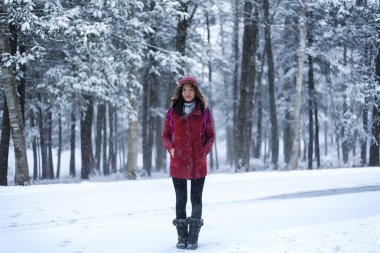 Kışın Torrington, Connecticut 'taki Burr Pond Eyalet Parkı' nda kar yağışı altında kırmızı ceketli güzel bir Çinli kadın poz veriyor.. 
