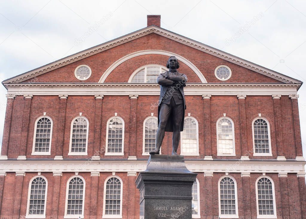 The red brick exterior architecture of the historic faneuil hall behind the samuel adam statue in Boston Massachusetts on an overcast day.