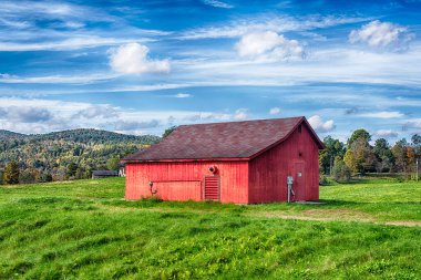 A red barn on a field landscape in the new england town of Cornwall connecticut on a blue sky day.
