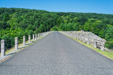 Thomaston Barajı 'nın tepesinde Litchfield County' deki Thomaston Connecticut 'ta güneşli mavi bir gökyüzü gününde asfalt bir yol..  
