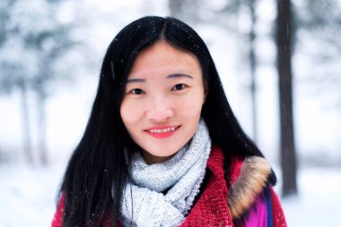 A chinese woman smiling outside in a winter scene in New England light snow.