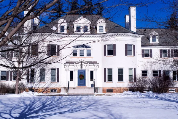 A large white victorian style mansion in the town of stockbridge massachusetts on a sunny winter day.