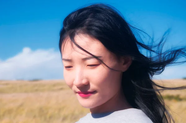 A chinese woman with hair blowing in the wind within the national seashore scenic area in Cape Cod Massachusetts on a sunny blue sky day.