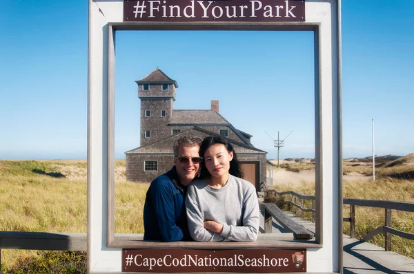 A man and woman couple framed in the cape cod national seashore with the old harbor life saving station in the background in provincetown massachusetts.