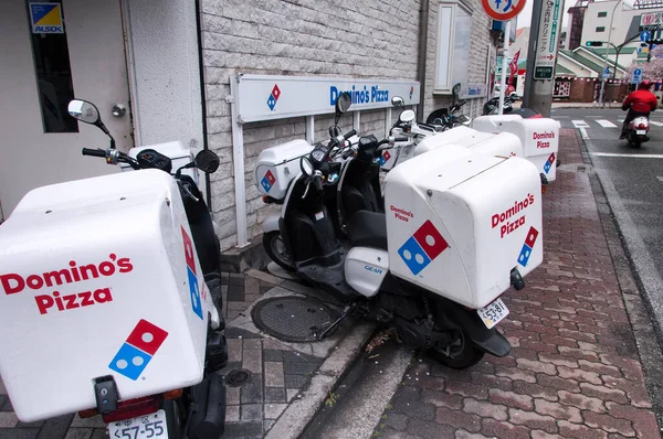 Yokohama, Japan.  April 7, 2019.  Dominos Pizza delivery scooters parked on a sidewalk within the city of Yokohama Japan on an overcast day.  