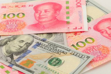 Chinese 100 Renminbi and 100 U.S. dollar bills piled on a white background.  