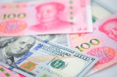 Chinese 100 Renminbi and 100 U.S. dollar bills piled on a white background.  