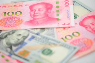 Chinese 100 Renminbi and 100 U.S. dollar bills piled on a white background.  