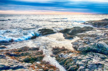 Newport Rhode Island 'ın kayalık kıyıları Birleşik Devletler' de alacakaranlıkta mavi gökyüzü ve beyaz bulutların altında.