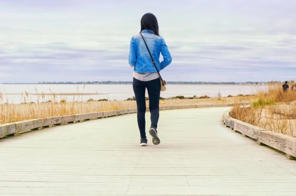 A Chinese woman walking on a boardwalk between Silver Sands State Park and Walnut Beach in Milford Connecticut on an overcast day.