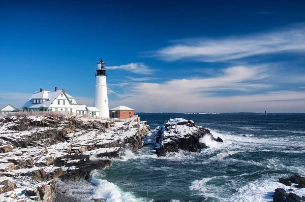 the iconic landmark Portland Headlight after a winter storm in Portland Maine on a sunny blue sky day.