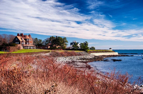 The rocky coast and cliffwalk of Newport Rhode Island in the united states under blue sky and white clouds.