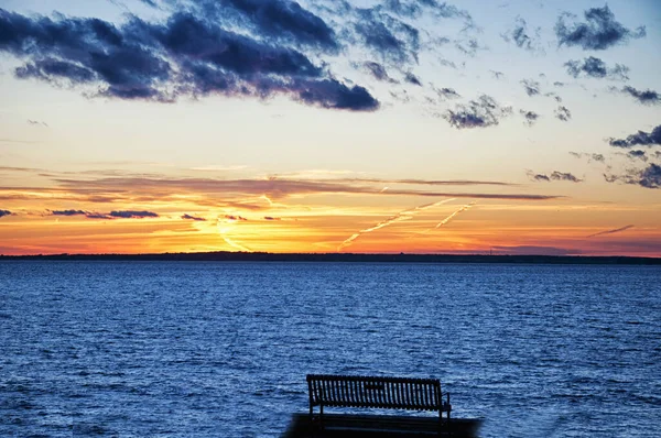 A solitary park bench overlooking a beautiful sunset on the atlantic ocean on ocean drive in newport Rhode island. 