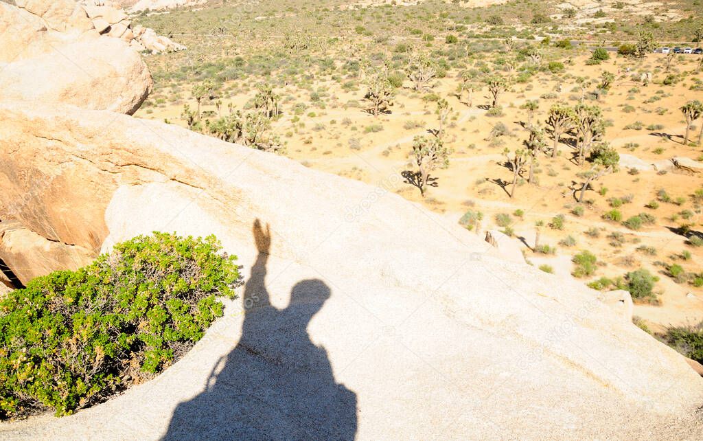 A man's shadow climbing rocks within the hall of horrors area of Joshua Tree National Park in an arid desert in California. 