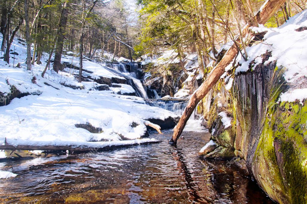 A small stream flowing down through Enders State Forest in Granby Connecticut on a sunny winter day.