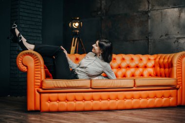 A business woman in a formal suit lies on an orange sofa 
