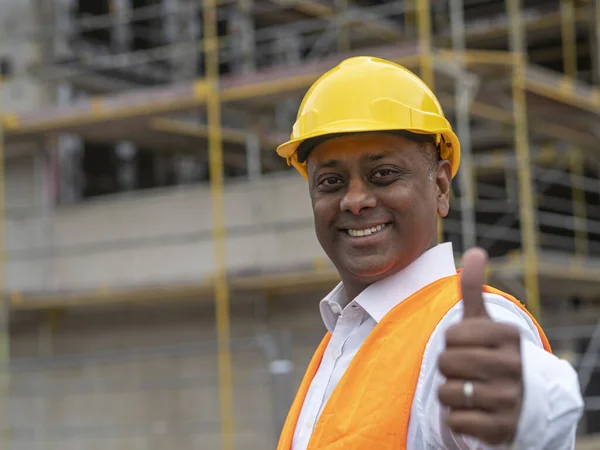 Positive, smiling and successful Indian construction worker posing looking at the camera and showing a thumbs up gesture