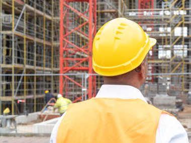 İnşaat alanı, geleceğe bakıyor. Güvenlik ceketi ve kasketi olan bir inşaat işçisi.