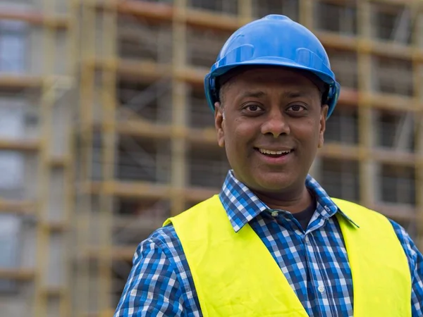 Portrait of a smiling Indian civil engineer or factory worker wearing a blue helmet and looking at camera