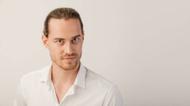 Genç sarışın sakallı adam kameraya bakıyor. Moda saçı olan beyaz bir adamın portresi kopya alanı olan beyaz bir stüdyonun arka planında izole edilmiş.