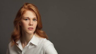 Beyaz gömlek giyen genç kızıl saçlı kadın. Koyu gri arka planda izole edilmiş kadın model stüdyo resmi. Mükemmel makyaj ve saç stili.
