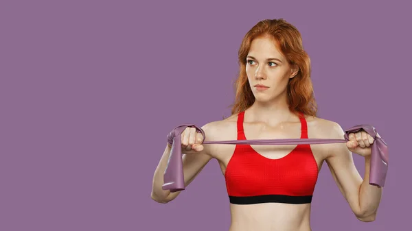 Home fitness. Young athlete woman warms up using rubber resistance band. Studio shot isolated against solid background