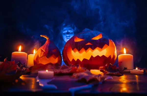 Kürbisse im Rauch mit geschnitzten Gesichtern bei Kerzenschein mit einem blauen Geist. — Stockfoto