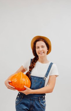 Çiftçi beyaz bir arka planda duruyor ve elinde bir portakal kabağı tutuyor..